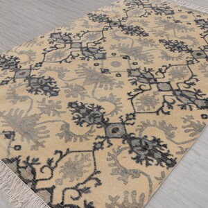 Puede incluir: Una alfombra beige con un patr&oacute;n geom&eacute;trico negro y gris. La alfombra tiene un borde de flecos.