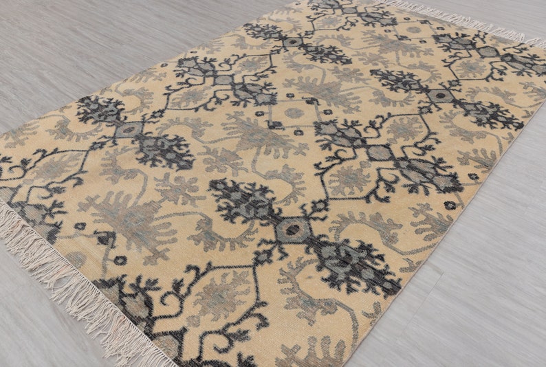 Puede incluir: Una alfombra beige con un patr&oacute;n geom&eacute;trico negro y gris. La alfombra tiene un borde de flecos.