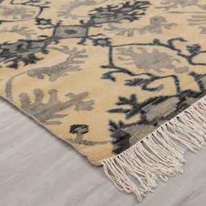 Puede incluir: Una alfombra beige con un patr&oacute;n geom&eacute;trico azul y negro. La alfombra tiene un borde de flecos.