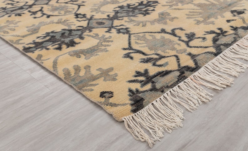 Puede incluir: Una alfombra beige con un patr&oacute;n geom&eacute;trico azul y negro. La alfombra tiene un borde de flecos.