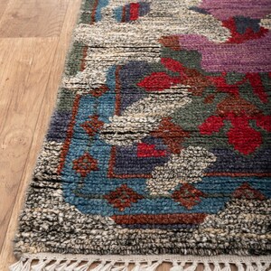 May include: A hand-woven rug with a colorful floral pattern in shades of blue, red, green, and purple. The rug has a fringe border and is made of wool.