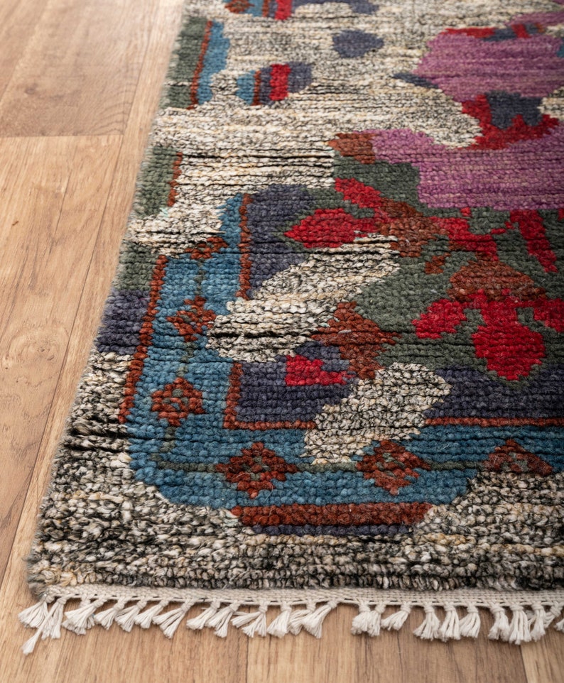 May include: A hand-woven rug with a colorful floral pattern in shades of blue, red, green, and purple. The rug has a fringe border and is made of wool.