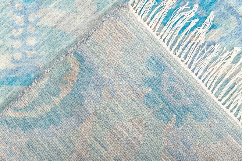 Puede incluir: Una alfombra tejida azul y blanca con un borde de flecos. La alfombra tiene un patr&oacute;n sutil de azul claro y oscuro.