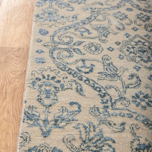 K&ouml;nnte beinhalten: Ein beiger Teppich mit einem blauen Blumenmuster. Der Teppich hat einen Fransenrand.