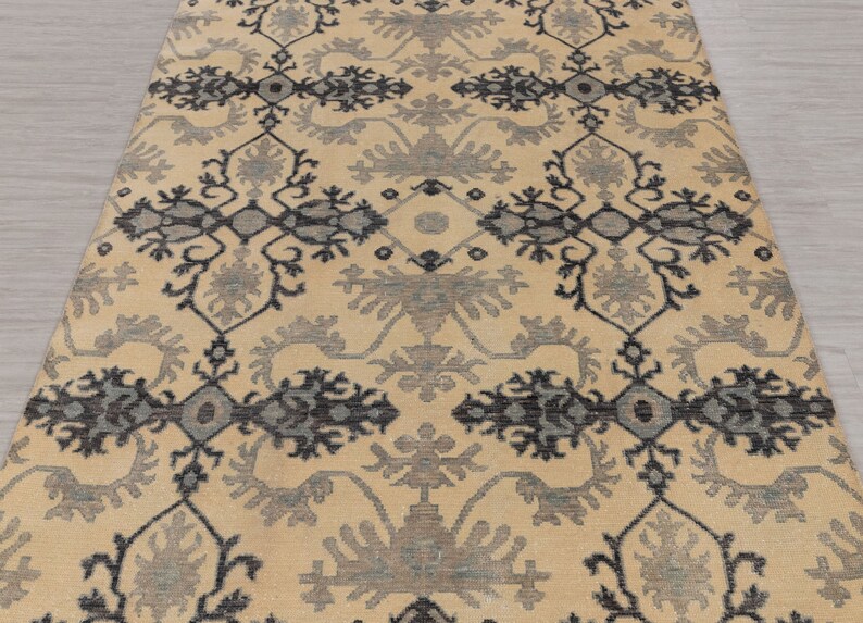 Puede incluir: Una alfombra beige con un patr&oacute;n geom&eacute;trico negro y gris. La alfombra tiene un dise&ntilde;o tradicional con detalles intrincados.