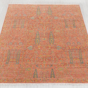 May include: A rectangular, rust-colored rug with an intricate pattern of stylized trees and floral elements in shades of blue, yellow, and green. The rug has a fringe along the edges and is suitable for home decor.