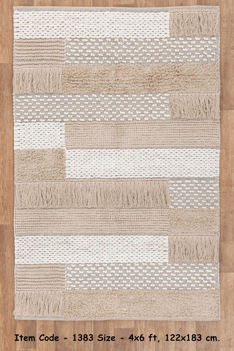 May include: A beige and white woven rug with a geometric pattern and fringe. The rug is 4x6 feet or 122x183 centimeters.