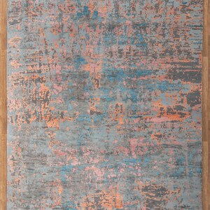 K&ouml;nnte beinhalten: Rechteckiger Teppich mit einem Used-Look-Design. Der Teppich hat eine graue Grundfarbe mit Akzenten in Blau, Rosa und Orange. Er hat einen Fransenrand und misst 250x300 cm.
