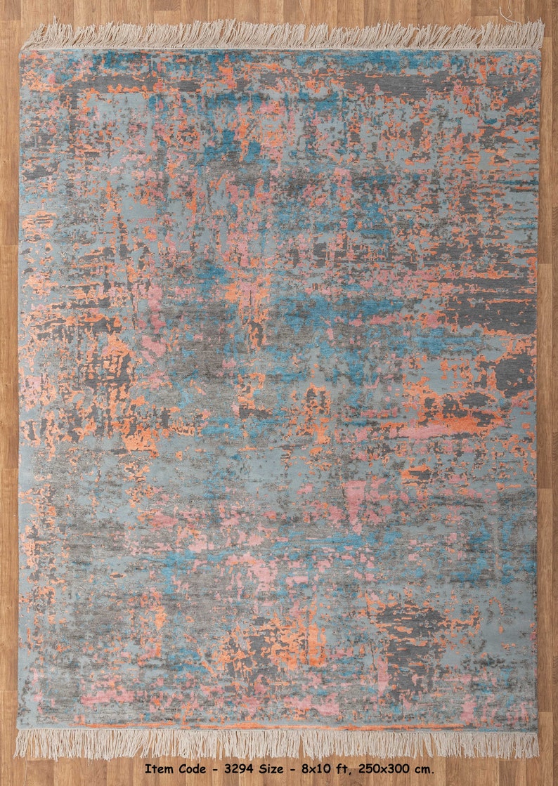 K&ouml;nnte beinhalten: Rechteckiger Teppich mit einem Used-Look-Design. Der Teppich hat eine graue Grundfarbe mit Akzenten in Blau, Rosa und Orange. Er hat einen Fransenrand und misst 250x300 cm.