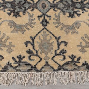 Puede incluir: Una alfombra beige con un patr&oacute;n floral negro y gris. La alfombra tiene un borde de flecos.