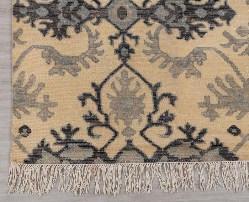 Puede incluir: Una alfombra beige con un patr&oacute;n floral negro y gris. La alfombra tiene un borde de flecos.
