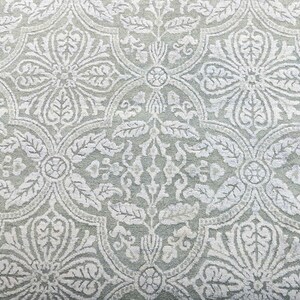 May include: A close-up of a light gray fabric with a white floral pattern. The pattern is intricate and features a repeating design of leaves and flowers.