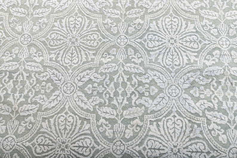May include: A close-up of a light gray fabric with a white floral pattern. The pattern is intricate and features a repeating design of leaves and flowers.