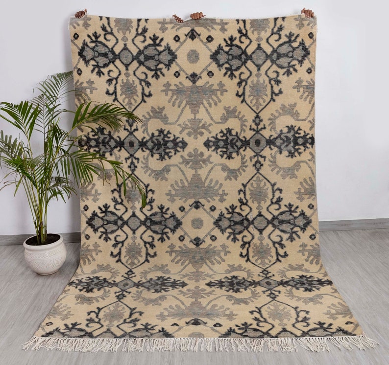 Puede incluir: Una alfombra de color crema con un patr&oacute;n geom&eacute;trico negro y gris. La alfombra tiene un borde de flecos.