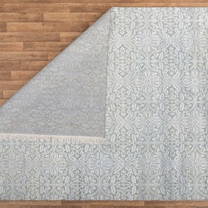 May include: A light gray area rug with a white floral pattern. The rug has a fringe border.