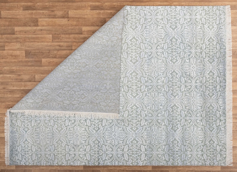 May include: A light gray area rug with a white floral pattern. The rug has a fringe border.