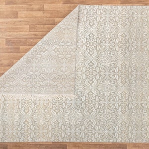 Puede incluir: Una alfombra blanca con un delicado patr&oacute;n floral y flecos en los bordes. La alfombra est&aacute; doblada por la mitad, revelando el patr&oacute;n en ambos lados.