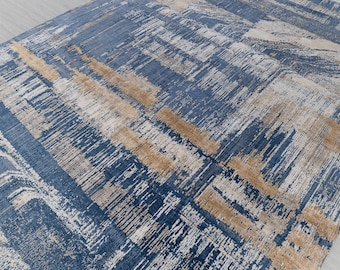 Puede incluir: Alfombra de área abstracta con un esquema de color azul, beige y dorado. La alfombra tiene un diseño moderno y contemporáneo con un aspecto texturizado y tejido.