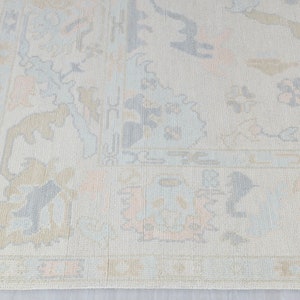 May include: A light beige rug with a subtle pattern of light blue and peach floral designs. The rug has a fringe border.