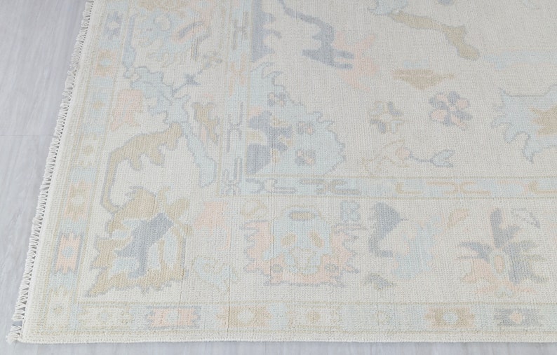 May include: A light beige rug with a subtle pattern of light blue and peach floral designs. The rug has a fringe border.