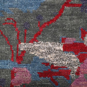 May include: Close-up of a colorful rug with a geometric pattern. The rug features shades of blue, red, white, and pink. The pattern is abstract and resembles a stylized floral design.