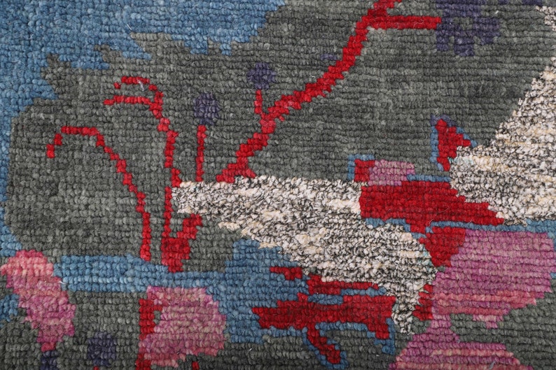 May include: Close-up of a colorful rug with a geometric pattern. The rug features shades of blue, red, white, and pink. The pattern is abstract and resembles a stylized floral design.