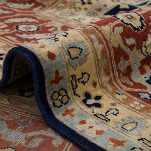May include: Close-up of a rug with a detailed floral pattern in shades of red, blue, and beige. The rug has a navy blue border.