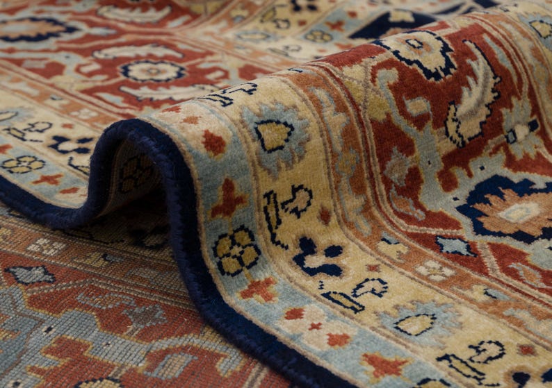 May include: Close-up of a rug with a detailed floral pattern in shades of red, blue, and beige. The rug has a navy blue border.
