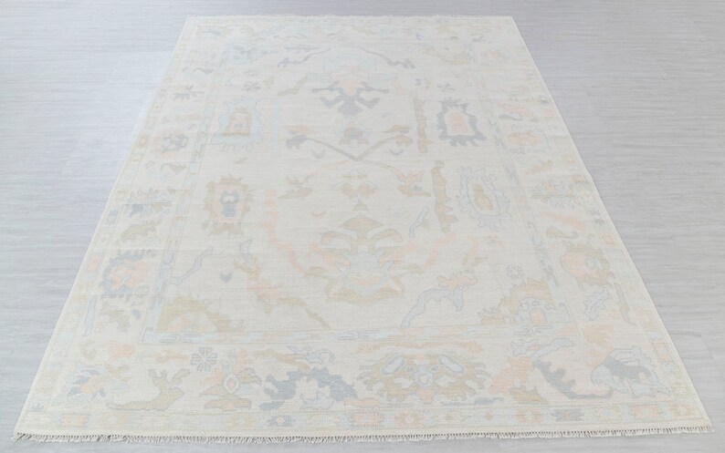 May include: A cream-colored rug with a traditional Persian design in shades of light blue, peach, and beige. The rug has a fringe border.