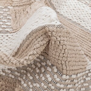May include: A close-up of a beige and white woven rug with a textured, bumpy surface. The rug has a geometric pattern with different sized squares and rectangles.