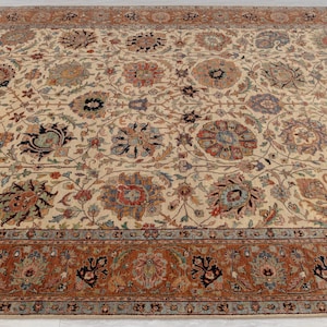 May include: A cream-colored rug with a floral pattern and a brown border. The rug has a traditional design with intricate details.