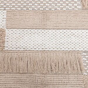 May include: A beige and white woven rug with a patchwork design. The rug has a fringe border and is made of different textures.