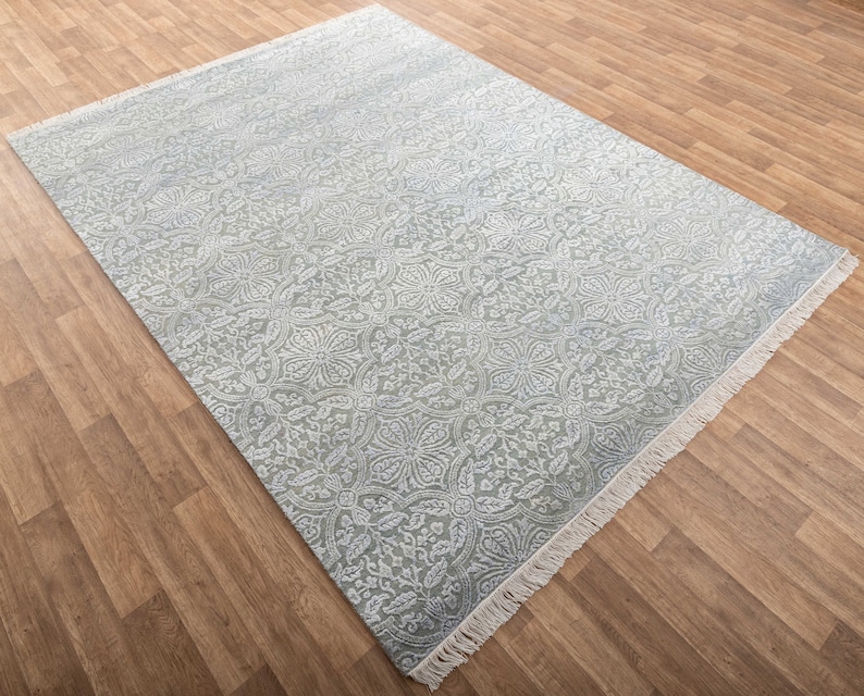 May include: A light blue rug with a white floral pattern. The rug has a fringe border.
