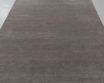 May include: A close-up of a brown area rug with a subtle textured pattern. The rug has a smooth, even surface and a slightly darker border.