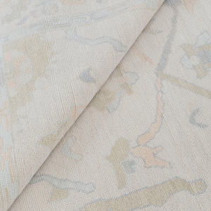 May include: A close-up of a light beige rug with a subtle pattern of light blue and peach floral designs.