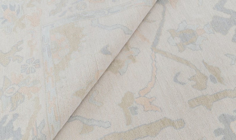 May include: A close-up of a light beige rug with a subtle pattern of light blue and peach floral designs.
