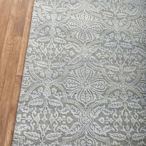 May include: A light green rug with a white floral pattern and a fringe border.