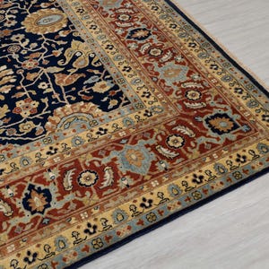 May include: A navy blue rug with a detailed floral pattern in shades of red, gold, and blue. The rug has a border with a repeating pattern of small flowers and leaves.