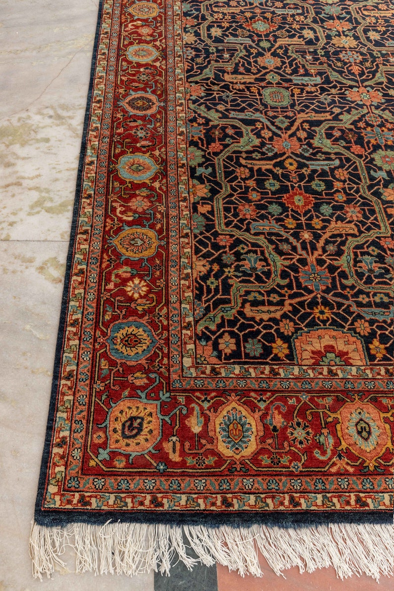 May include: A traditional Persian rug with a dark blue background and intricate floral patterns in shades of red, orange, and green. The rug has a white fringe border.