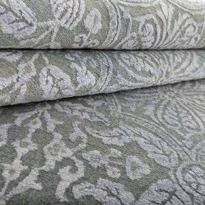 May include: Close-up of a folded, light blue rug with a white, intricate floral pattern.
