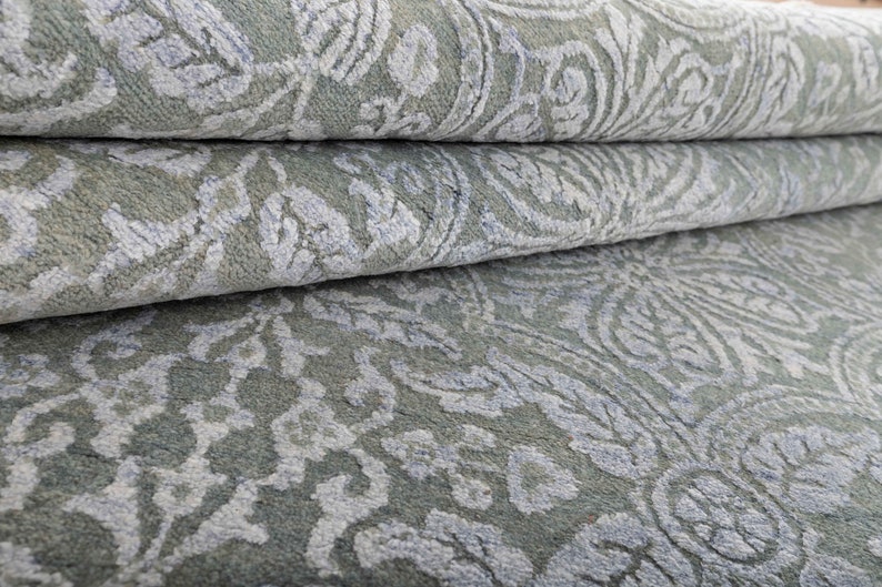 May include: Close-up of a folded, light blue rug with a white, intricate floral pattern.