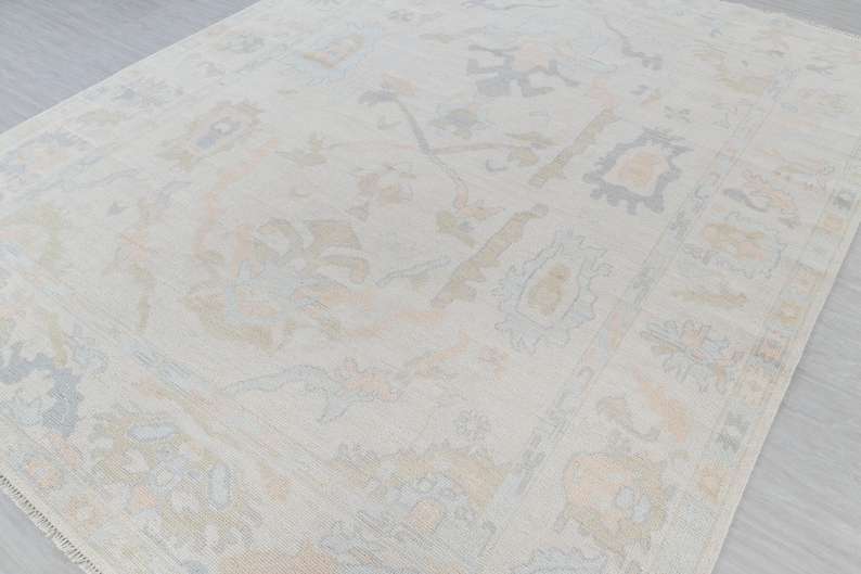 May include: A light beige rug with a subtle, intricate pattern in shades of light blue, peach, and beige. The pattern features floral and geometric motifs.