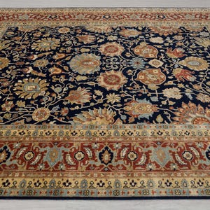 May include: A navy blue rug with a floral pattern in shades of beige, brown, and red. The rug has a border with a repeating pattern of geometric shapes.