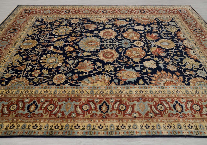 May include: A navy blue rug with a floral pattern in shades of beige, brown, and red. The rug has a border with a repeating pattern of geometric shapes.