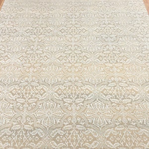 Puede incluir: Una alfombra beige con un intrincado patr&oacute;n floral blanco. La alfombra tiene un brillo sutil y una textura suave.
