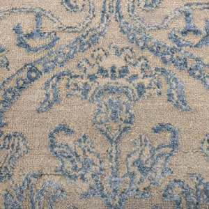 K&ouml;nnte beinhalten: Nahaufnahme eines beigen Teppichs mit einem blauen Blumenmuster. Der Teppich hat eine weiche, strukturierte Oberfl&auml;che.