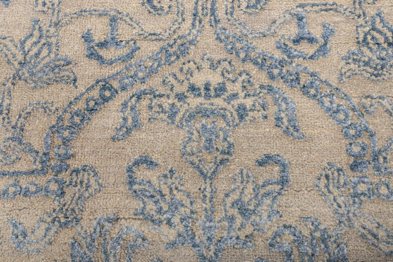 K&ouml;nnte beinhalten: Nahaufnahme eines beigen Teppichs mit einem blauen Blumenmuster. Der Teppich hat eine weiche, strukturierte Oberfl&auml;che.