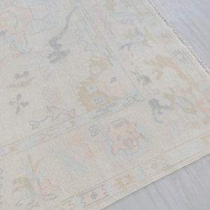 May include: A light beige rug with a subtle floral pattern in shades of light blue and pink. The rug has a fringed edge.