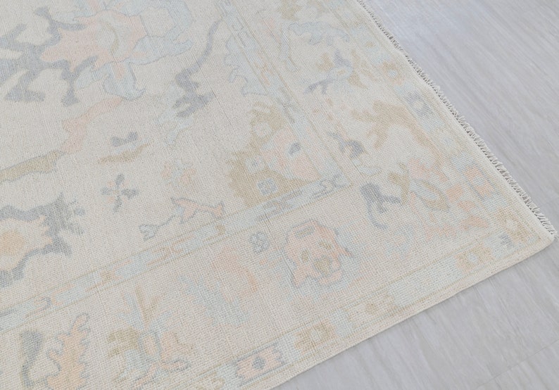 May include: A light beige rug with a subtle floral pattern in shades of light blue and pink. The rug has a fringed edge.