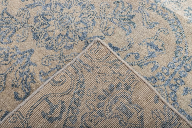 K&ouml;nnte beinhalten: Nahaufnahme der R&uuml;ckseite eines Teppichs mit einem blauen und beigen Muster. Der Teppich hat eine gewebte Textur und einen Fransenrand.
